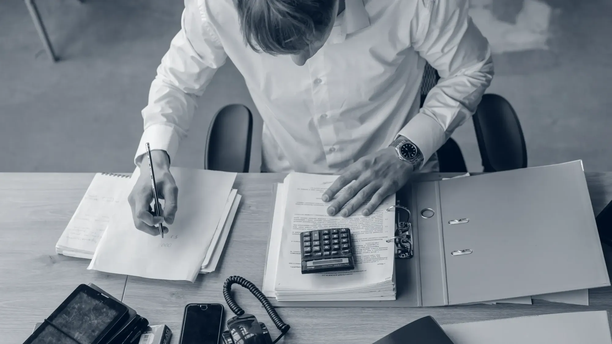 A dealer manager at a desk reviewing service contract paperwork with a calculator and binder